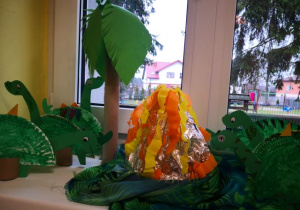 Wystawa prac dzieci przedstawiająca dinozaury i wulkan.