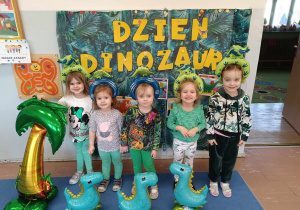 Dzieci z grupy 3-4 latków stoją w grupie. W tle dekoracja