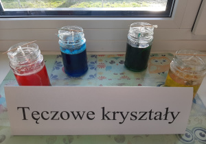 Doświadczenie "Tęczowe kryształy". W czterech słoikach z kolorową wodą wymieszaną ze solą umieszczono nitki wełny, na których wytrącają się solne kryształki.