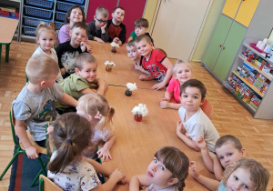 Dzieci siedzą przy stolikach. W wazonikach umieszczają kwiaty. Przygotowują doświadczenie "Kolorowe kwiaty".