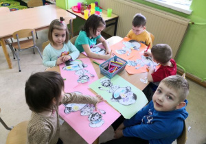Przedszkolaki siedzą przy stoliku i wykonują pracę plastyczną "Marcowa pogoda".