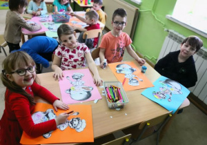 Przedszkolaki siedzą przy stoliku i wykonują pracę plastyczną "Marcowa pogoda".