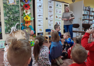 Dzieci w bibliotece słuchają opowieści pani bibliotekarki o dinozaurach.