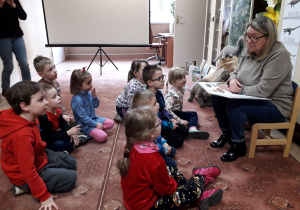 Dzieci w bibliotece słuchają opowieści pani bibliotekarki o dinozaurach.
