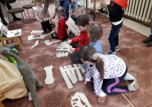 Dzieci układają szkielet dinozaura z wielu elementów.