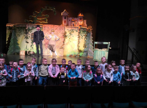 Dzieci pozują do zdjęcia grupowego przed sceną w teatrze.