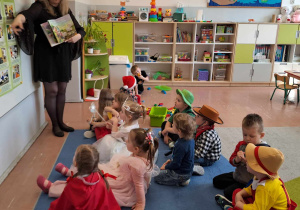 Dzieci siedzą na dywanie i słuchają nauczycielki