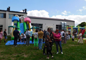 Dzieci skaczą na dmuchanym zamku, rodzice obserwują swoje pociechy.