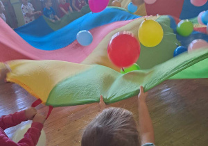 Dzieci ustawione dookoła chusty na której są balony