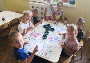 Przedszkolaki siedzą przy stoliku i malują obrazki.
