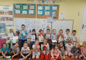 Grupa dzieci 5,6 - letnich pozuje do wspólnej fotografii, chłopcy prezentują krawaty od dziewczynek i dyplomy super chłopaka.