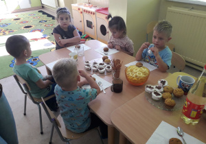 Dzieci przy stolikach ozdabiają babeczki.