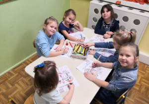 Dziewczynki siedzą przy stoliku i kolorują obrazek o prawach dziecka.