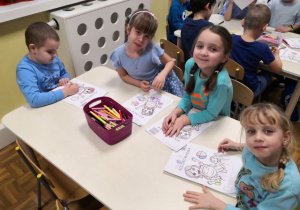 Dzieci siedzą przy stoliku i kolorują obrazek o prawach dziecka.