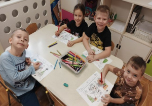 Dzieci siedzą przy stoliku i kolorują obrazki.