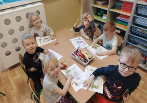 Dzieci siedzą przy stoliku i kolorują obrazki.