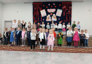 Przedszkolaki pozują do zdjęcia na tle dekoracji z okazji Dnia Babci i Dziadka.
