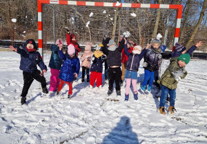 Dzieci stoją w bramce na boisku i rzucają śnieżkami