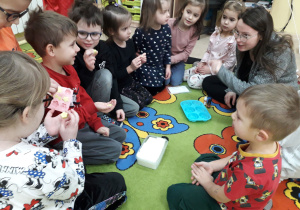 Dzieci na dywanie oglądają produkty potrzebne do produkcji mydełek.