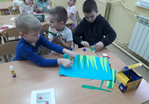 Chłopcy przy stoliku tworzą pracę plastyczną "Łąka Biedronki Piątki".