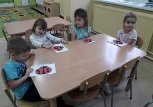 Dzieci przy stoliku prezentują wykonane biedronki.