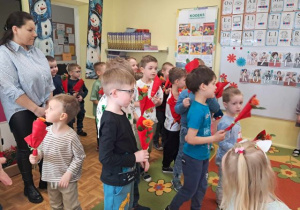 Chłopcy trzymają kwiatki i składają dziewczynkom życzenia.