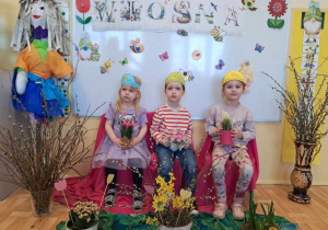 Troje dzieci pozuje do zdjęcia wśród wiosennej dekoracji.