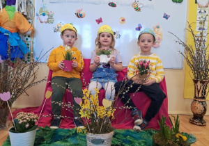 Troje dzieci pozuje do zdjęcia wśród wiosennej dekoracji.