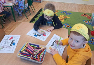 Chłopcy siedzą przy stoliku i kolorują chorągiewki na powitanie wiosny.