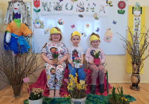 Troje dzieci pozuje do zdjęcia wśród wiosennej dekoracji.