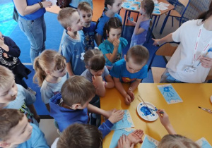 Przedszkolaki odbijają na dyplomach dłonie pomalowane niebieską farbą.
