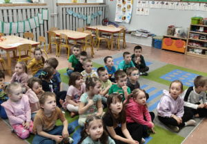 Dzieci siedzą na dywanie i słuchają opowiadania czytanego przez pedagoga
