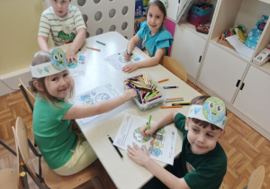 Dzieci siedzą przy stoliku i kolorują obrazek o ziemi.