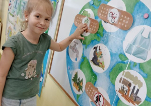 Dziewczynka dopasowuje obrazek przedstawiający właściwe zachowania ekologiczne do plakatu ziemi.