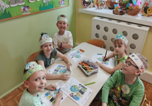 Dzieci siedzą przy stoliku i kolorują obrazek o ziemi.