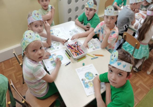 Dzieci siedzą przy stoliku i kolorują obrazek o ziemi.
