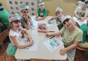 Dzieci siedzą przy stoliku i kolorują obrazek o ziemi.