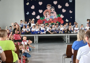 Dzieci siedzą na scenie i przygotowują się do występu z okazji Dnia Rodziny