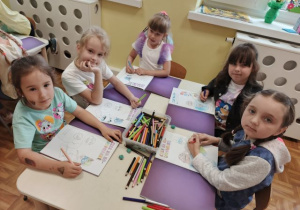Dziewczynki siedzą przy stoliku i wykonują karty pracy.