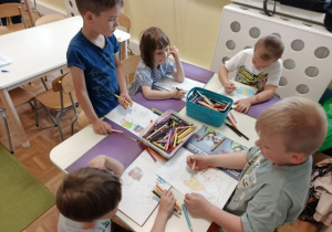 Przedszkolaki siedzą przy stoliku i wykonują karty pracy.