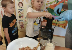 Dziewczynka wkłada owoce do wyciskarki soków.