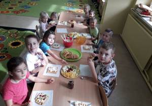 Dzieci przy stolikach prezentują wykonane przez siebie gofry.