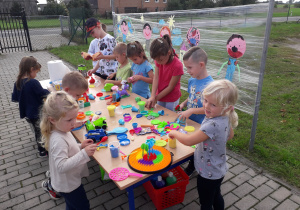 Dzieci przy stolikach bawią się ciastoliną.