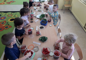 Dzieci przy stolikach kiszą pomidorki.