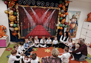 Przedszolaki siedzą w kole z paniami i prezentują zabawę z gumą sensoryczną.