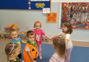 Dzieci tańczą w kole. W środku dziecko przebrane za dynię.