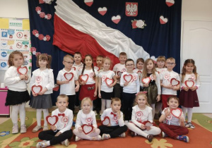 Grupa 5,6-latków pozuje do zdjęcia grupowego na tle flagi.