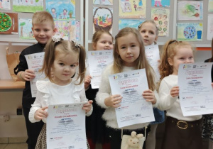 Laureaci konkursu pozują do zdjecia z dyplomami na tle prac konkursowych