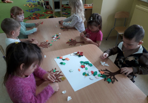 Dzieci przy stoliku ozdabiają drzewo jesiennymi , kolorowymi liśćmi.