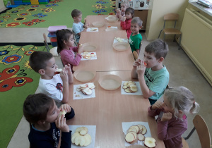 Dzieci przy stoliku kosztują jabłka.
